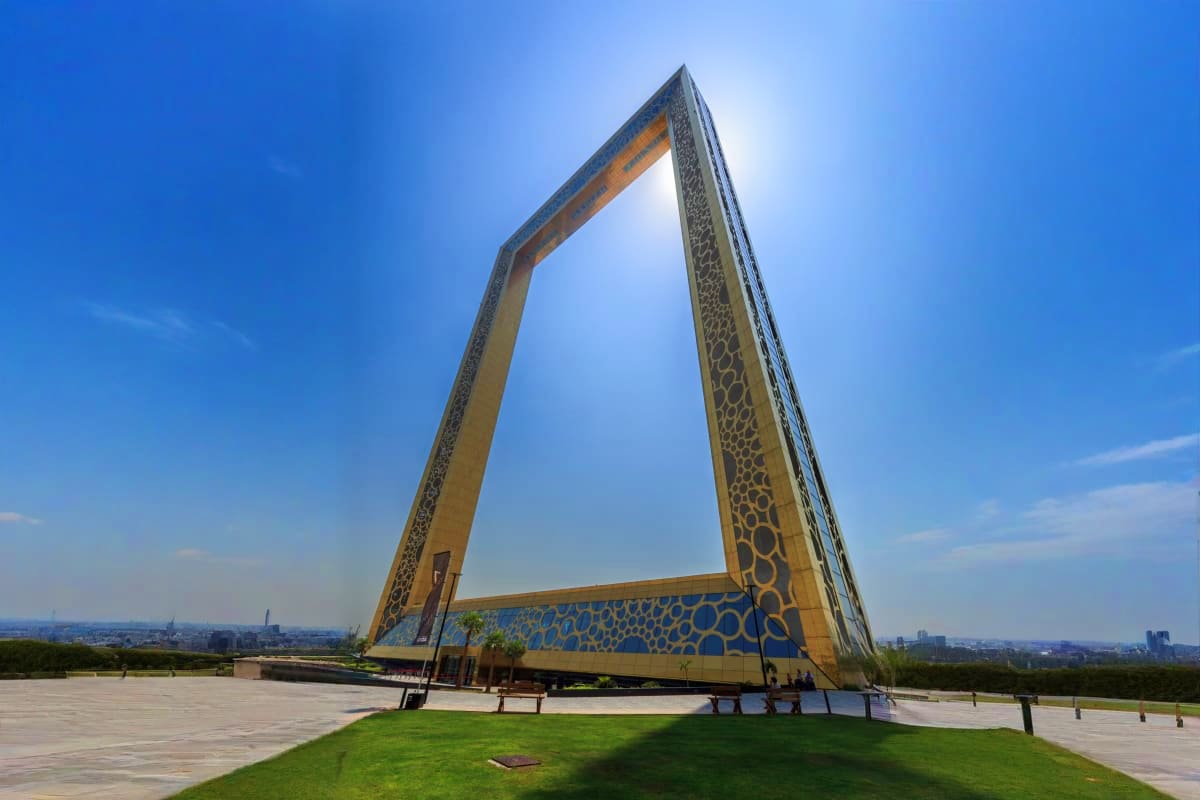Modern architectural monument with large golden frame structure and blue decorative patterns overlooking Dubai cityscape agai