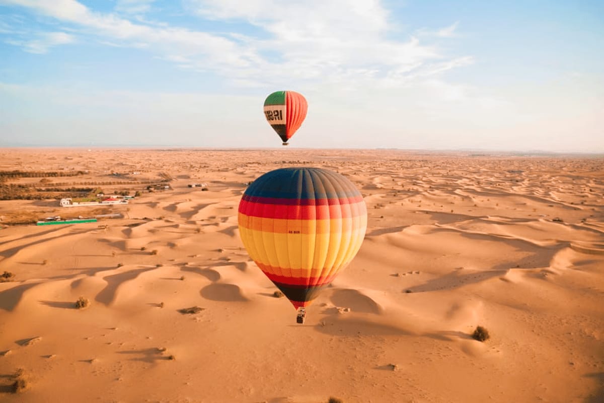 Hot air balloons floating above desert sand dunes during sunrise in Dubai