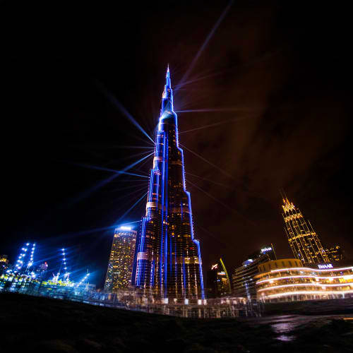 Burj Khalifa illuminated in blue at night with surrounding Dubai skyscrapers and golden-lit buildings in the background