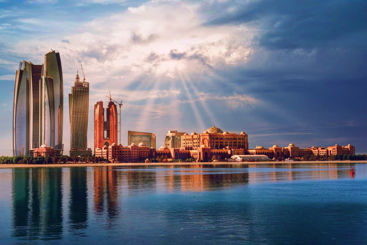 Abu Dhabi waterfront skyline at sunset with modern skyscrapers and traditional architecture reflected in calm water