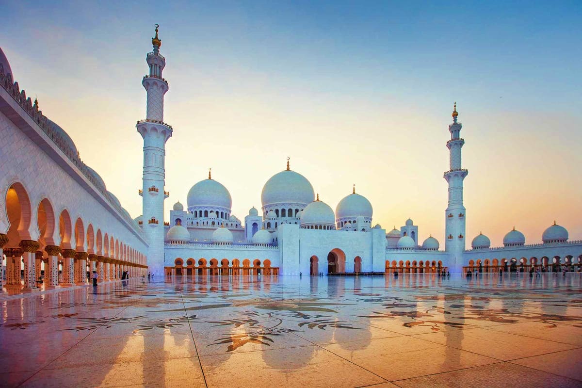 Sheikh Zayed Grand Mosque courtyard at sunset with white marble floors, blue domes, and ornate arches in Abu Dhabi