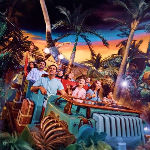 Family on Jungle Cruise ride at theme park with tropical sunset backdrop and palm trees