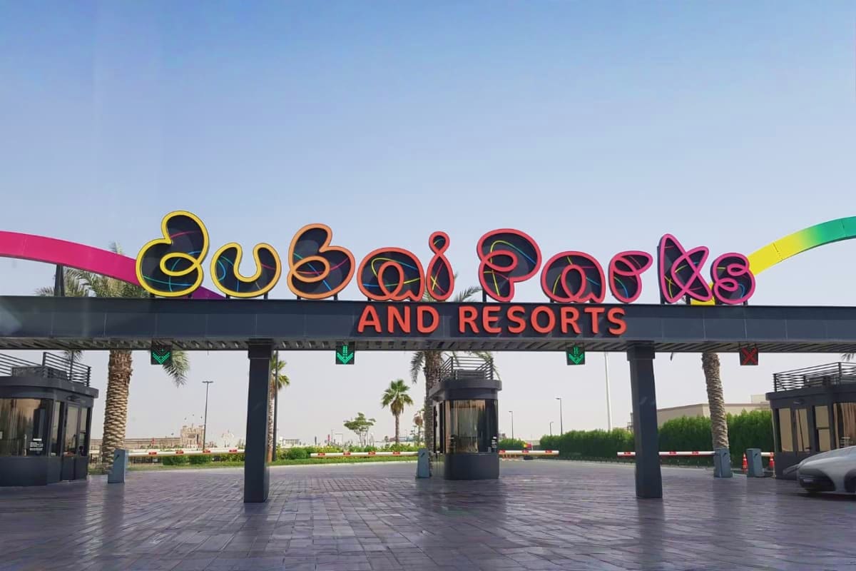 Dubai Kids Adventure and Theme Park Holiday Package Colorful neon sign for Dubai Parks and Resorts entrance with palm trees and modern architecture in background
