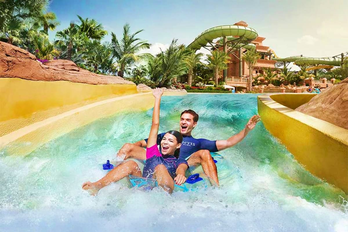 Couple riding a wave slide at a tropical water park with palm trees and waterslides in the background