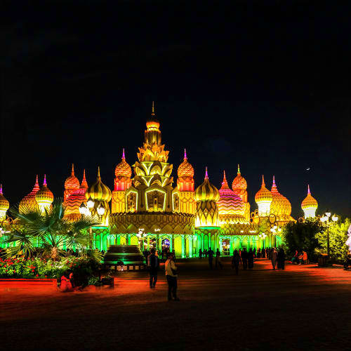 Illuminated Thai Buddhist temple at night with golden spires and colorful green lighting, featuring ornate architecture and d