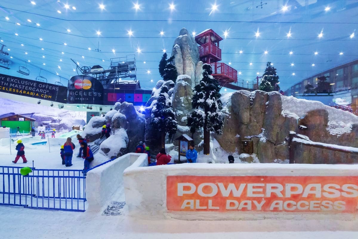 Dubai Sky Sea Adventure Escape Indoor ski resort with snow-covered trees, rock formations, and red cabin structure under starry ceiling lights with visitors