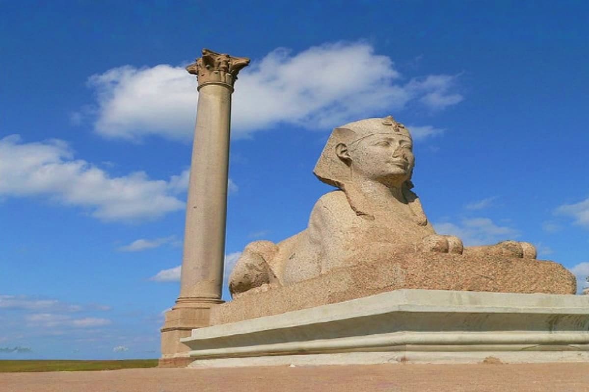Stone sphinx statue with decorative column against blue sky and flat desert landscape