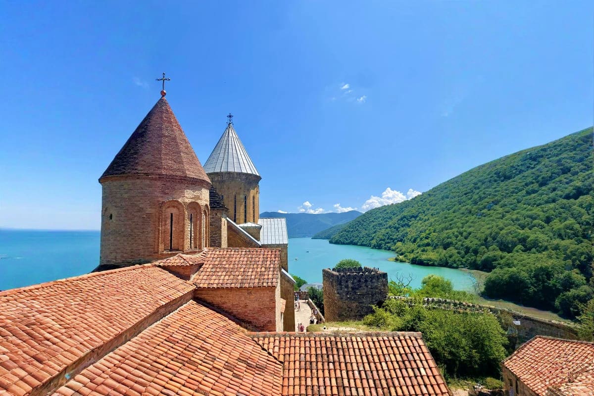 Historic Armenian church with conical domes and crosses overlooking turquoise lake surrounded by green forested mountains in 