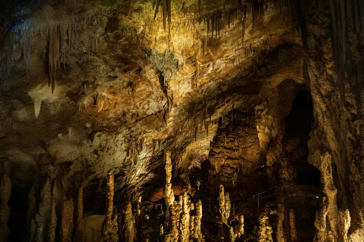 Illuminated limestone cave chamber with stalactites and stalagmites formations hanging from ceiling and rising from cave floo