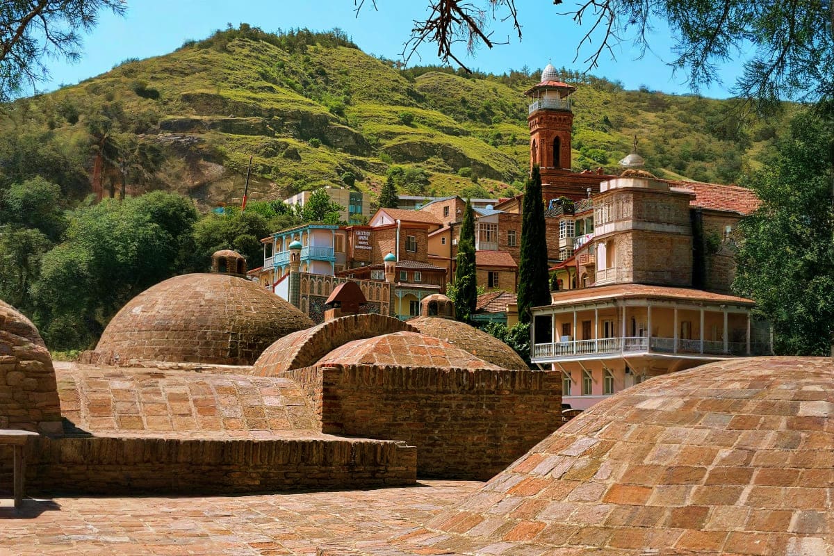 Historic Abanotubani bathhouses with domed roofs and brick architecture nestled against lush green hillside in Tbilisi, Georg