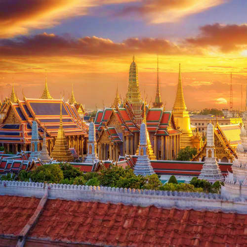 Grand Palace Bangkok at sunset with golden spires and traditional Thai temple architecture illuminated against orange sky