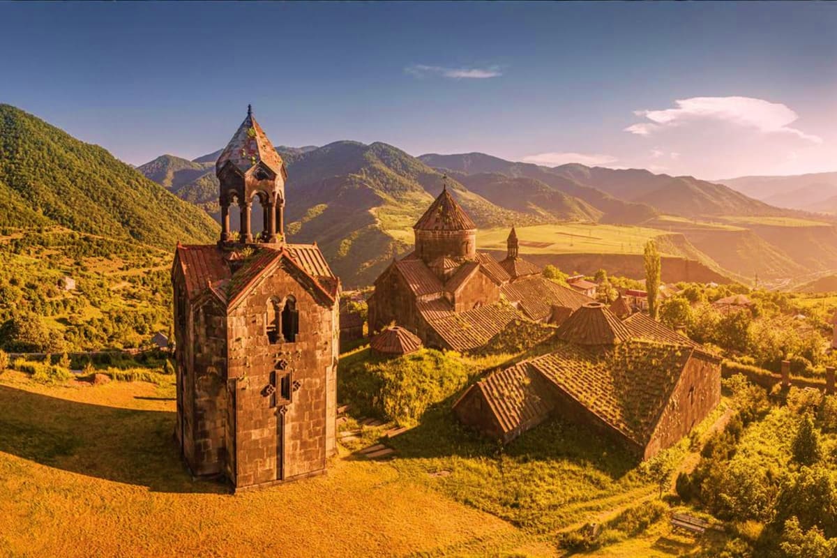 Ancient Armenian monastery complex with ornate stone churches and conical domes nestled in lush green mountains and golden va