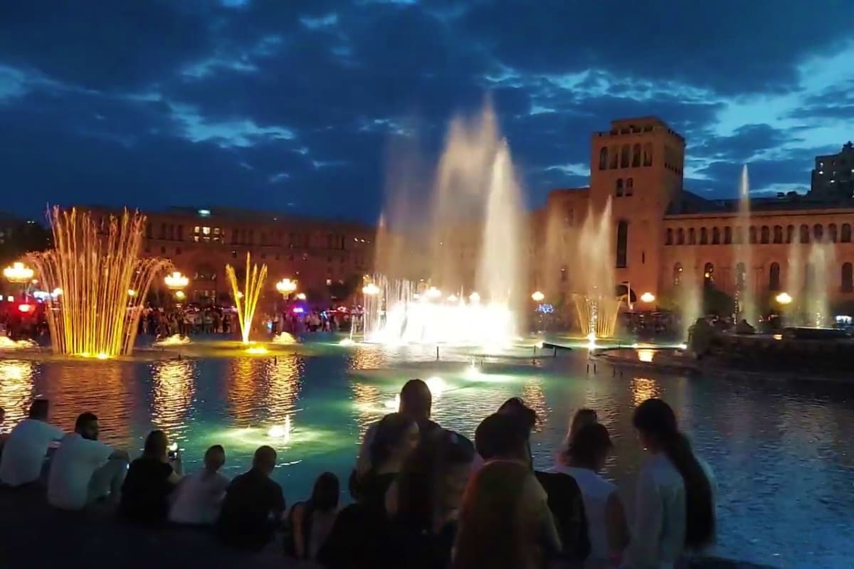 Illuminated fountain show at Republic Square in Yerevan, Armenia, at twilight with spectators watching and historic red build