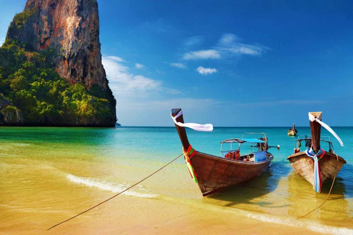 Thailand 4 City Island and Adventure Tour Traditional wooden longtail boats in turquoise water near limestone cliff in Thailand tropical beach destination