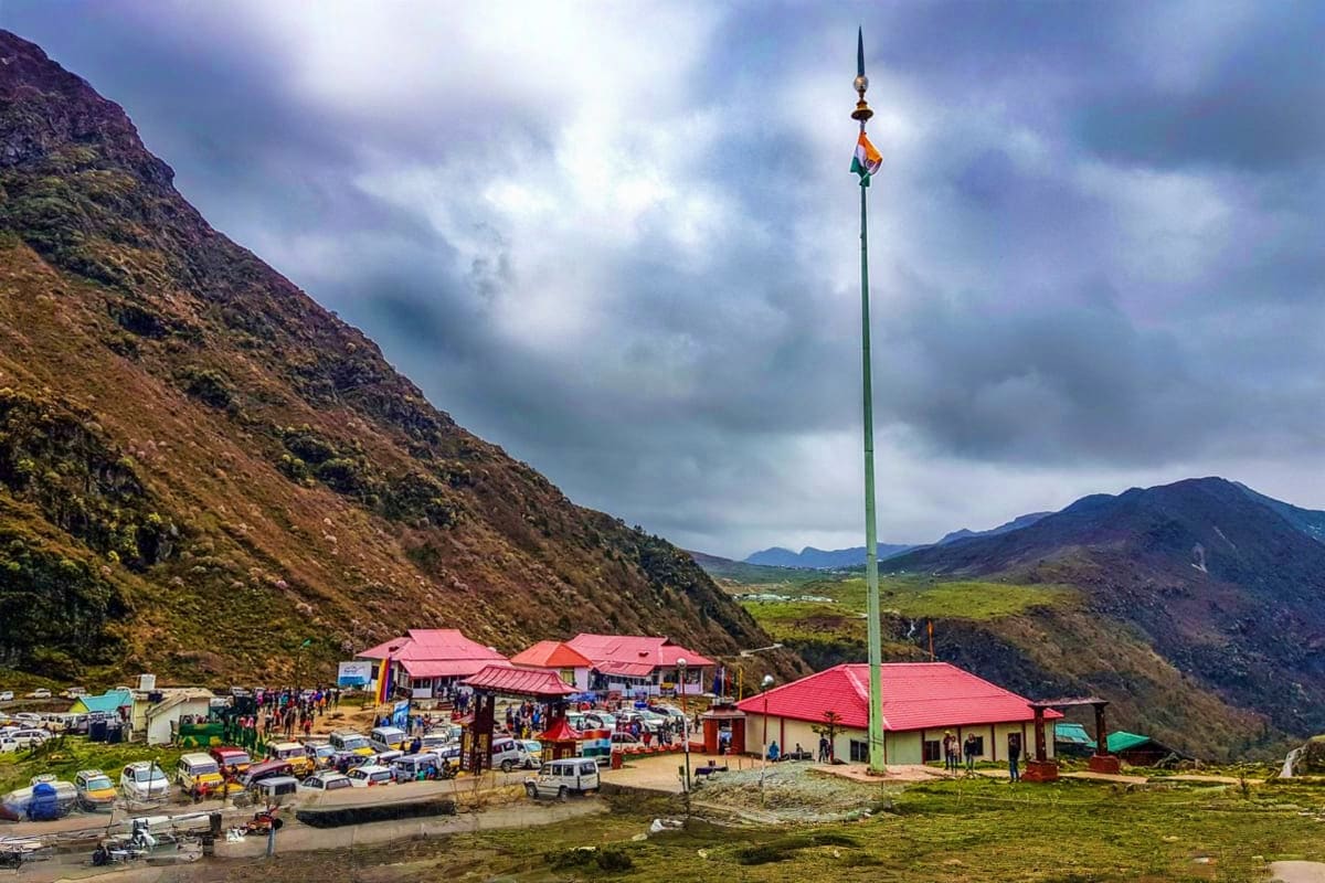 Mountain settlement in Sikkim with red-roofed buildings, Indian flag on tall pole, steep hillside, and valley landscape durin