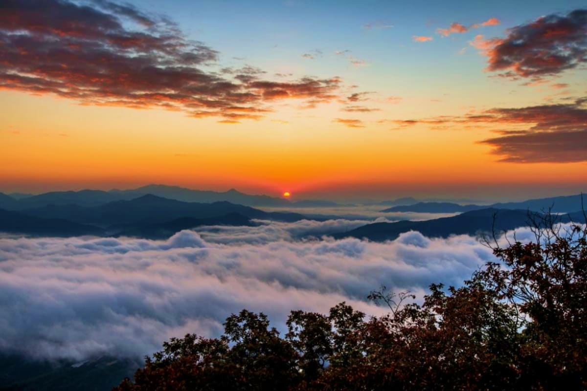 Sunrise over mountains with sea of clouds and silhouetted peaks, view from high elevation in Himalayan region