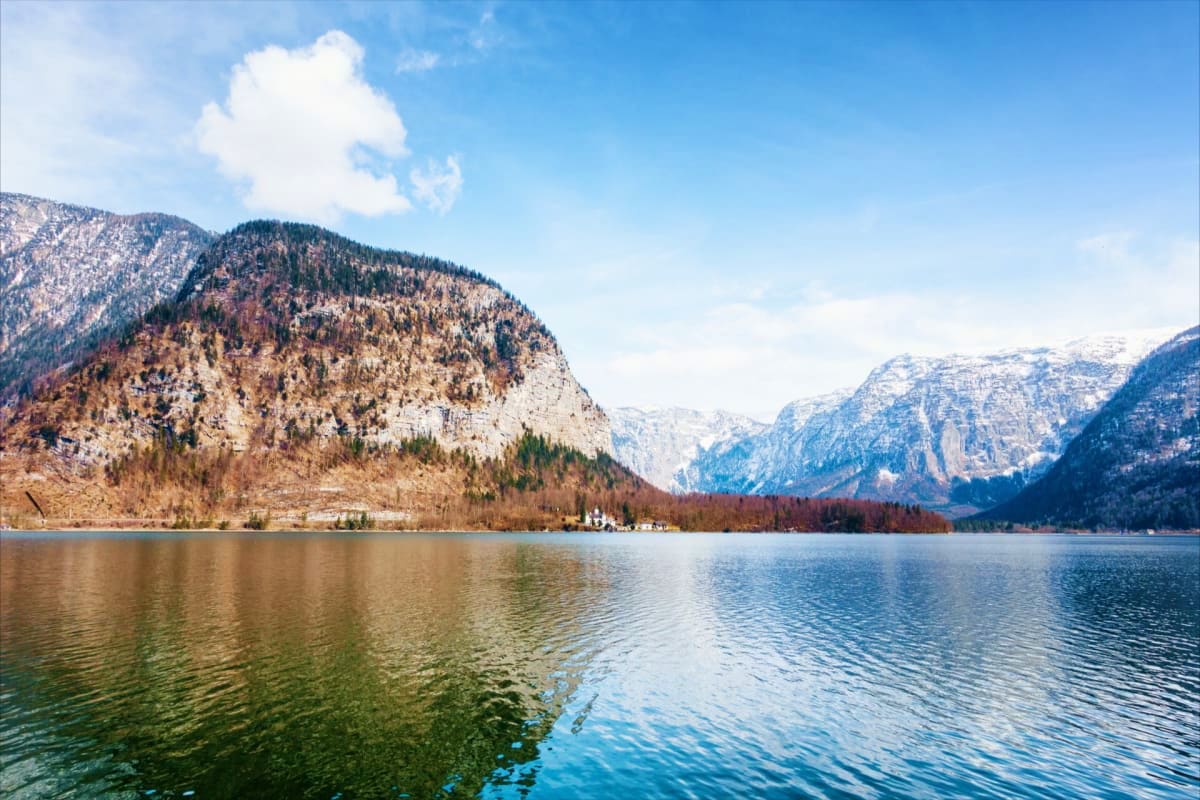 Alpine lake surrounded by snow-capped mountains and forested slopes under blue sky with white clouds