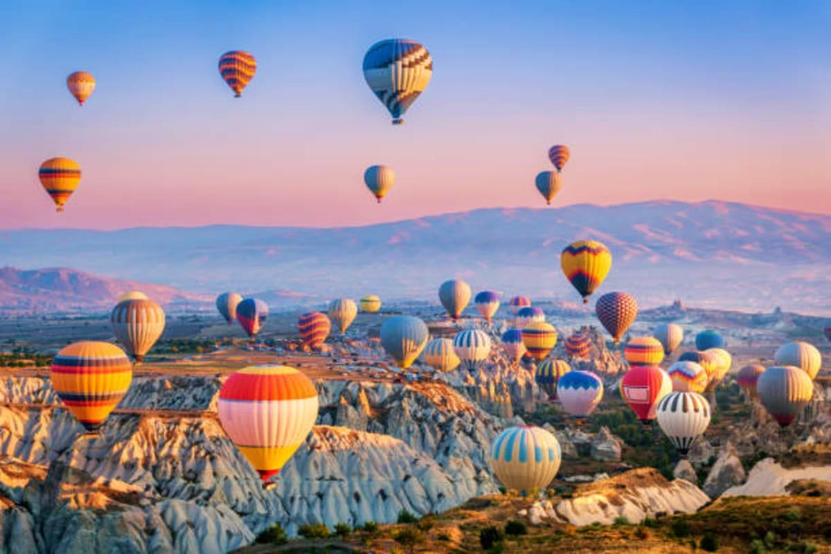 Multiple colorful hot air balloons floating over Cappadocia's distinctive white rock formations and valleys at sunrise