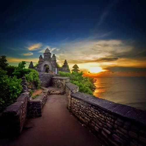 Ancient stone temple perched on clifftop overlooking ocean at golden sunset in Bali