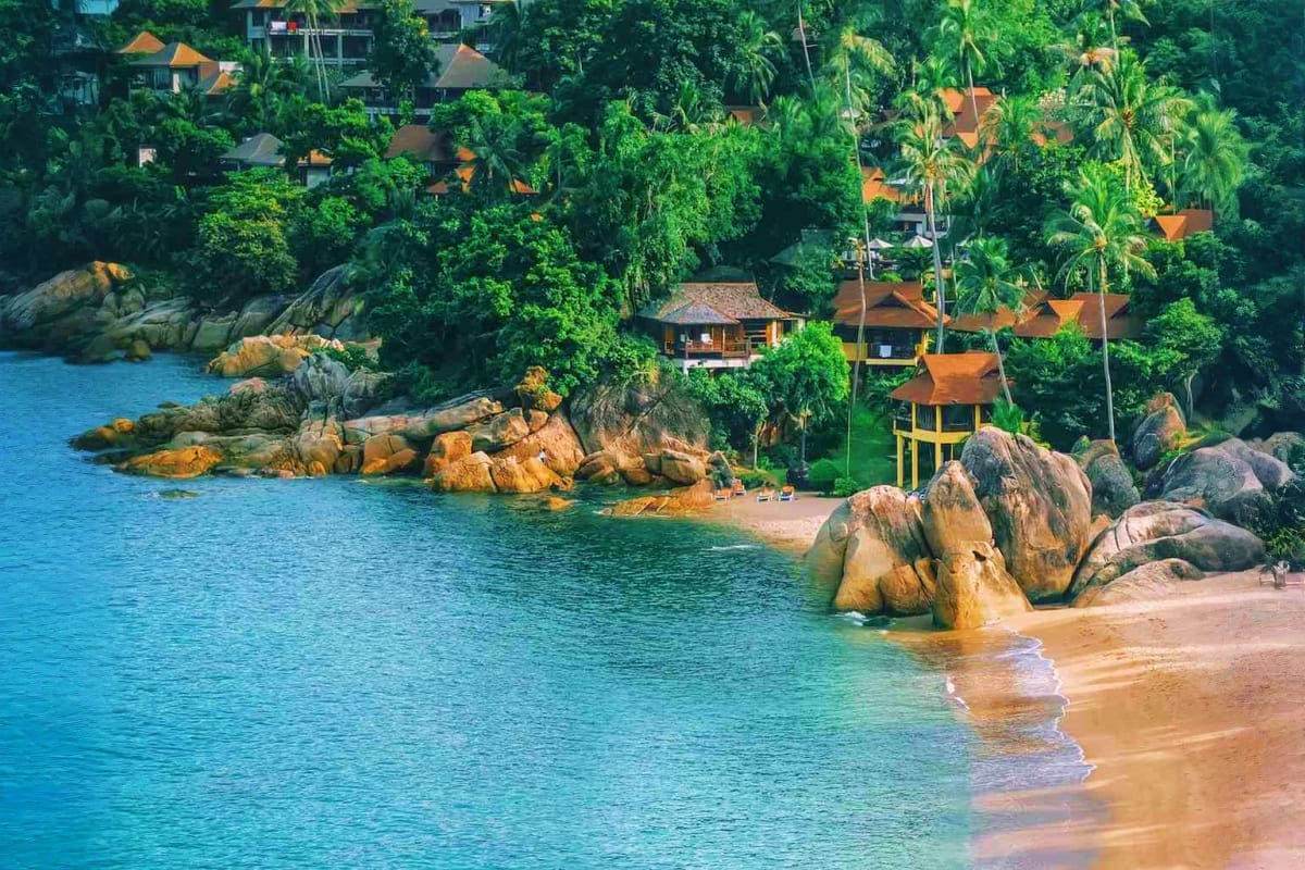 Tropical beach resort with golden-roofed bungalows nestled among palm trees, granite boulders, and turquoise waters in Southe
