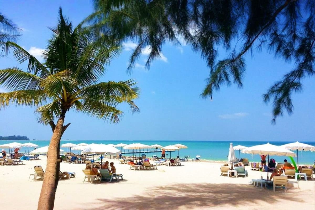 Tropical beach scene with white sand, palm tree, beach loungers, white umbrellas, and turquoise ocean water under blue sky