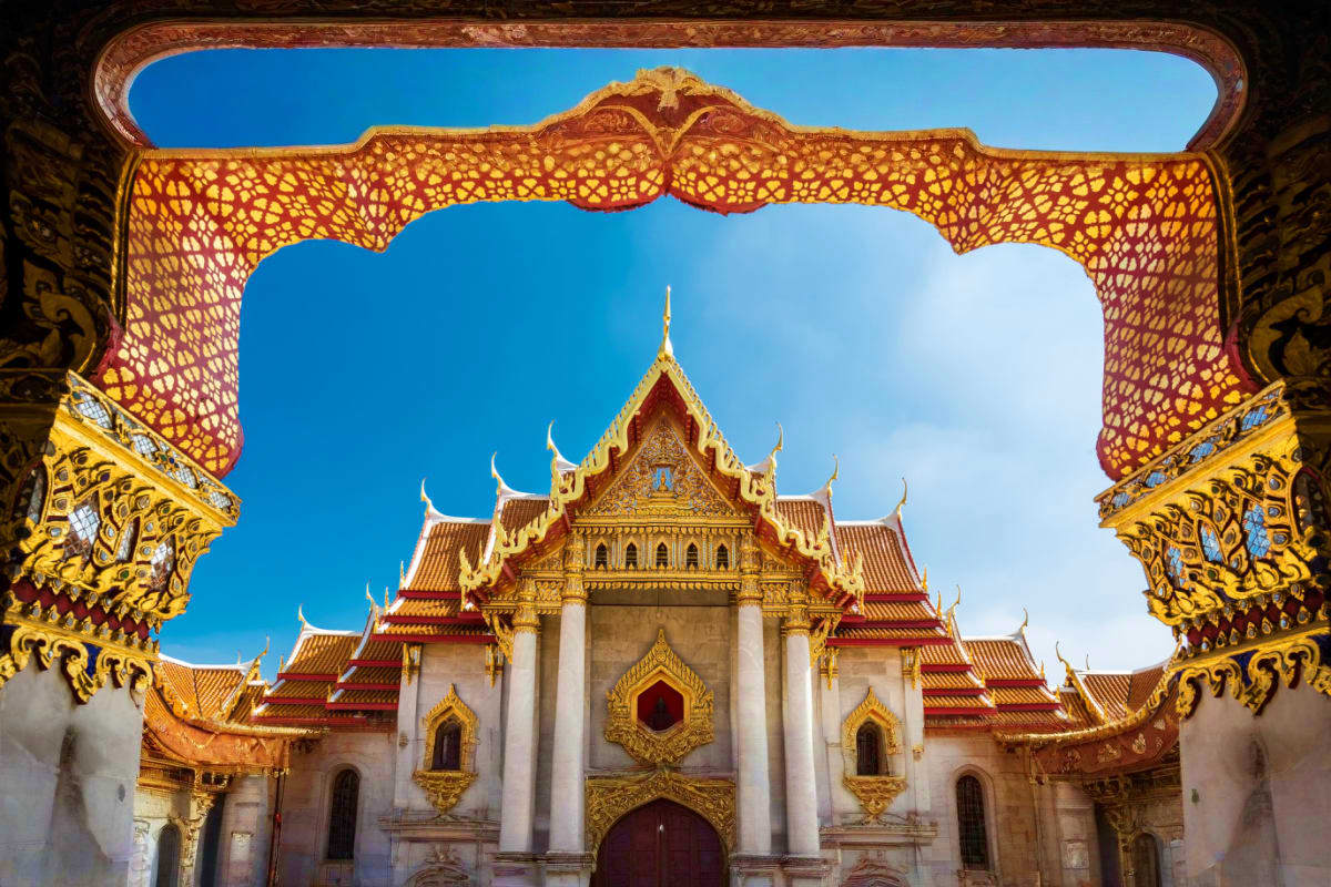 Ornate golden Buddhist temple with red-tiled roofs framed by decorative archway against blue sky