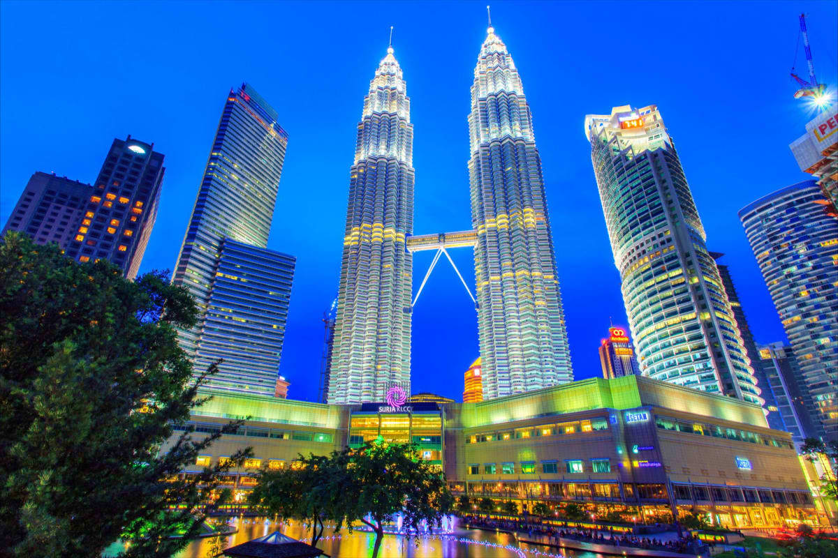 Petronas Twin Towers illuminated at twilight in Kuala Lumpur with surrounding skyscrapers and lit shopping mall below