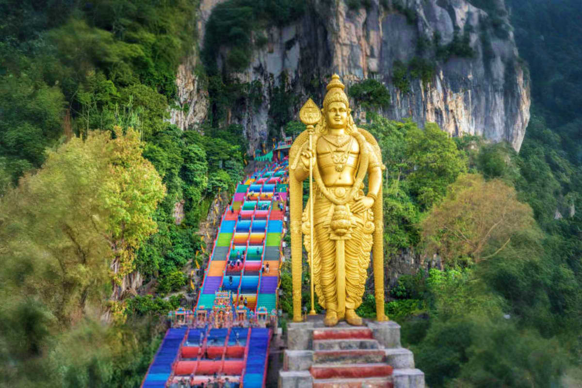 Giant golden Hindu statue at Batu Caves Malaysia with colorful rainbow staircase leading up to limestone cliff