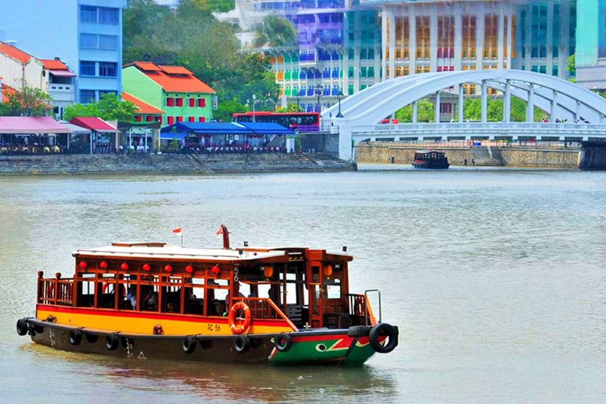 Traditional red and yellow wooden boat with red lanterns on river, white arch bridge and colorful buildings in background, Ma