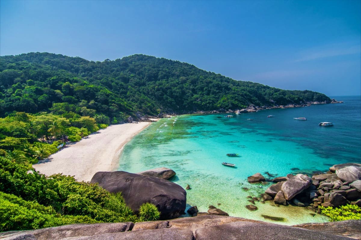 Scenic tropical beach with turquoise waters, white sand, granite boulders, and forested hillside in Andaman Islands