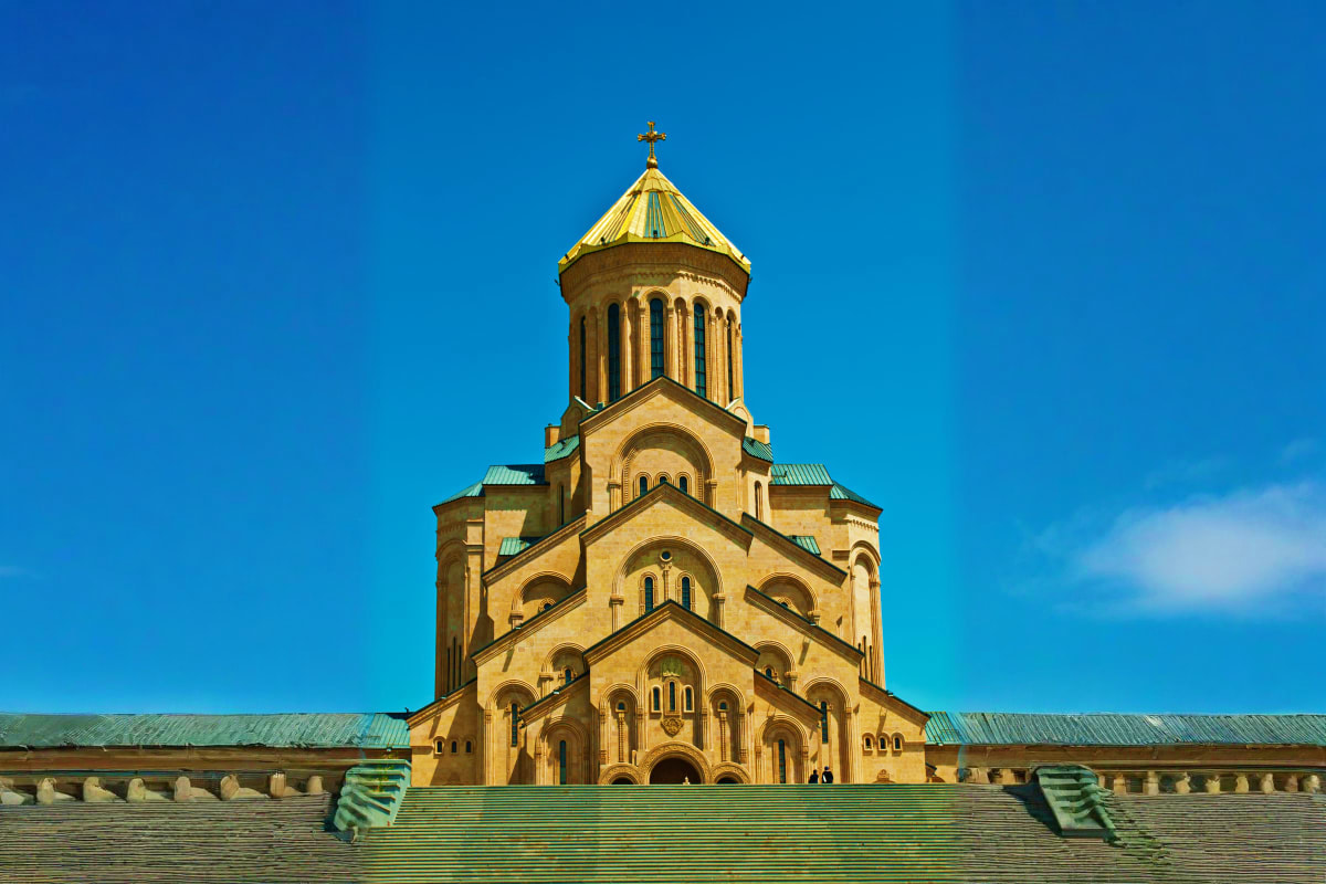 Georgian Orthodox church with golden dome and cross against clear blue sky, showcasing traditional religious architecture
