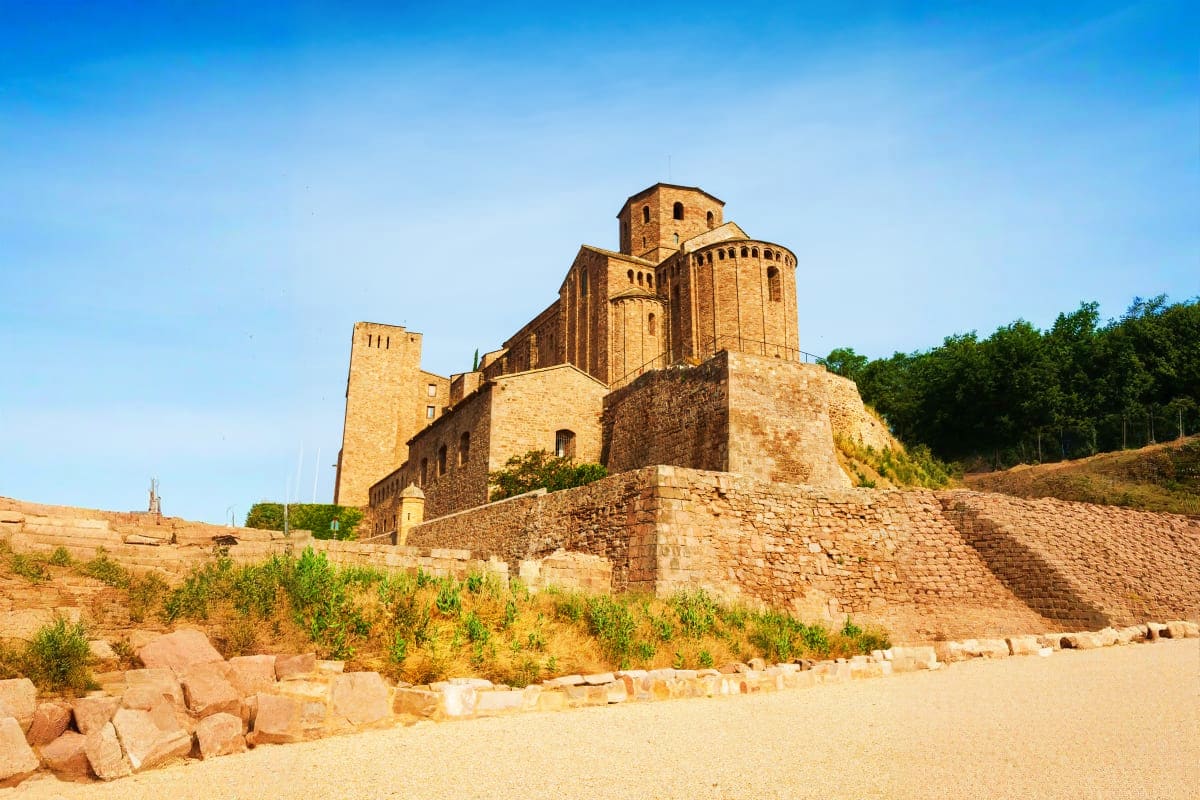 Medieval fortress with golden stone towers and defensive walls set on hillside with sparse vegetation and clear blue sky