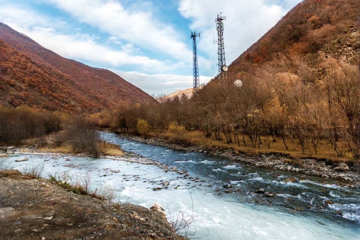 Mountain valley with flowing river, bare trees, and two tall telecommunications towers in Georgia landscape