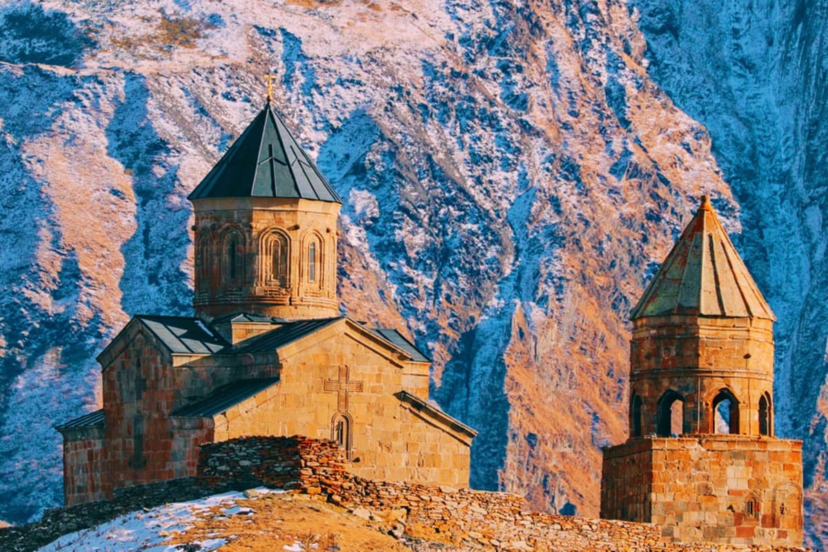 Ancient Armenian churches with conical domes nestled against dramatic blue and tan mountain cliffs in Georgia