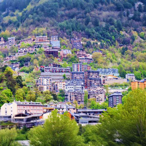 Urban hillside neighborhood with multi-story apartment buildings nestled among dense green forests and a river running throug