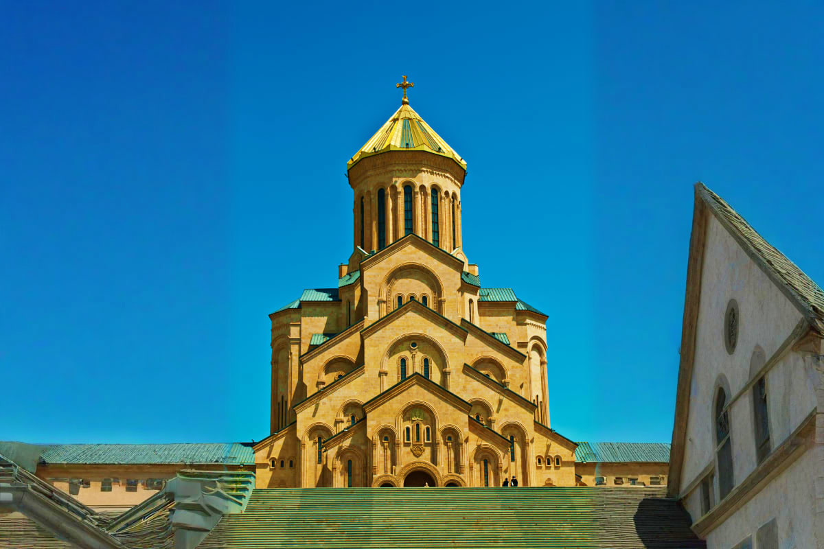 Golden domed Orthodox cathedral with cross on top against clear blue sky, surrounded by historic stone buildings