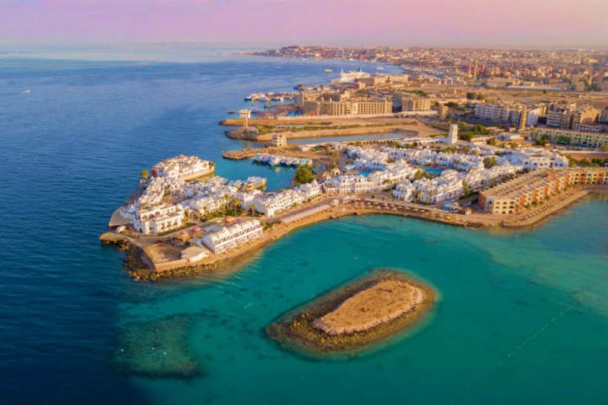 Aerial view of coastal resort town with white buildings, turquoise bay, and rocky islands along Mediterranean shore