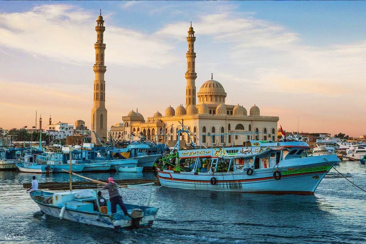 Traditional blue fishing boats in harbor with Al-Hakim Mosque and minarets at sunset in Alexandria, Egypt