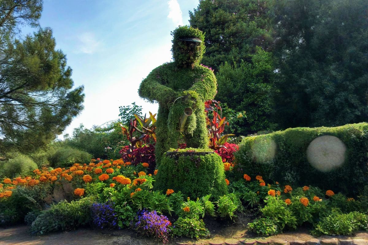 Large ivy-covered topiary sculpture with vibrant orange marigolds, red tropical flowers, and purple blooms in a botanical gar