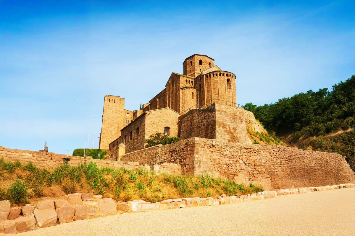 Ancient stone fortress with domed church towers on hillside overlooking sandy beach and vegetation in Georgia