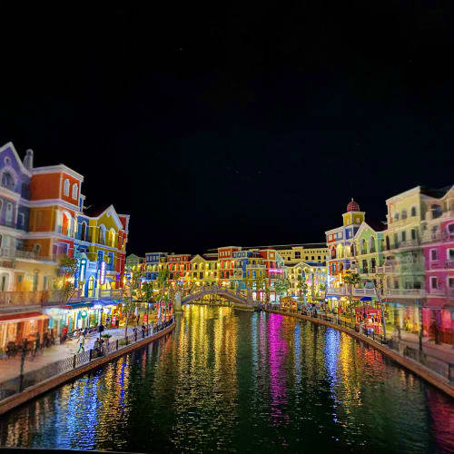 Colorful waterfront buildings reflecting in canal waters at night in Venice-inspired theme park with illuminated architecture