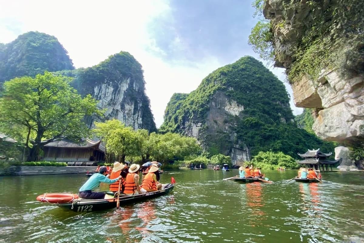 Tourists in orange life jackets rowing traditional wooden boats on a river surrounded by towering limestone karst mountains a