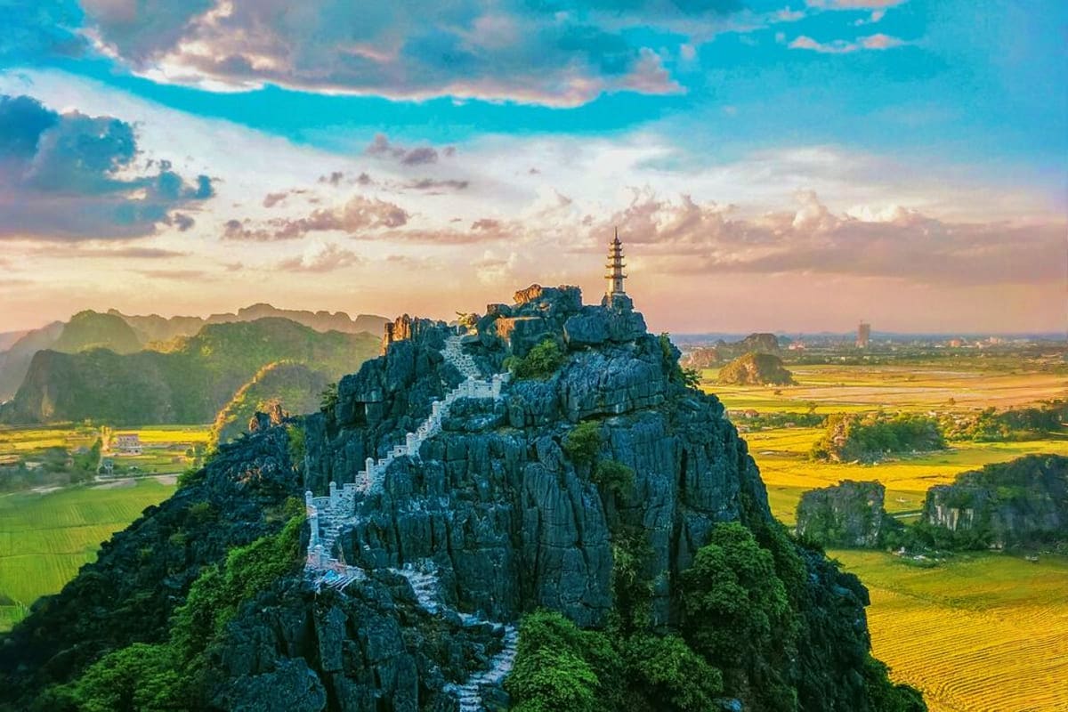 Mua Cave temple on limestone karst peak at sunset with golden rice fields and mountains in Ninh Binh, Vietnam