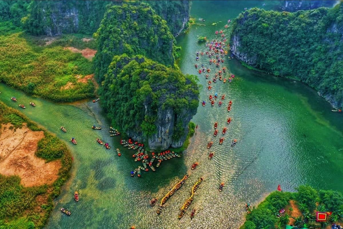Aerial view of Halong Bay with emerald waters, limestone karsts, and colorful tourist boats gathered among the rock formation