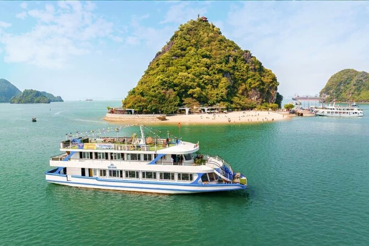 Luxury cruise boat with blue and white design in emerald waters near limestone island with beach and lush vegetation in Halon