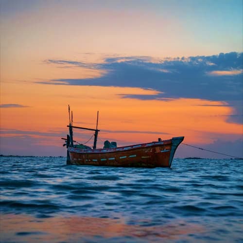 Traditional wooden fishing boat anchored in calm ocean waters during golden sunset with colorful sky