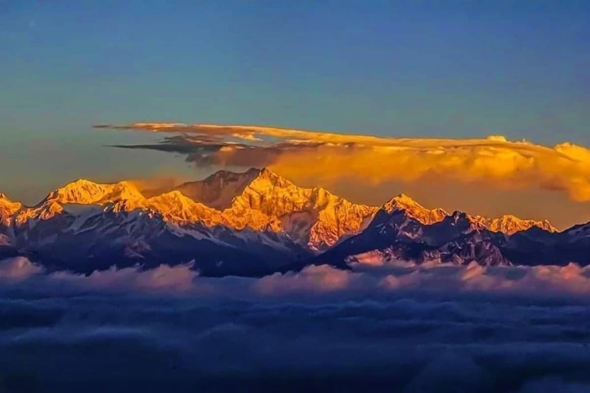 Snow-capped Himalayan mountain peaks glowing golden at sunrise above a sea of clouds in Darjeeling region