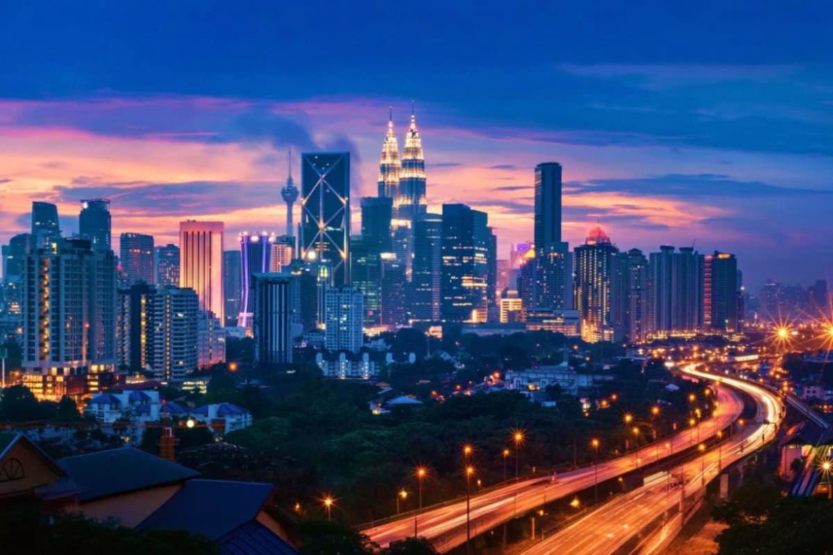 Kuala Lumpur skyline at dusk with illuminated Petronas Twin Towers, cityscape, and curved highway with light trails below