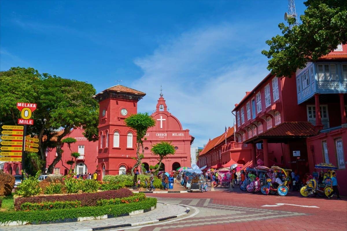 Christ Church Melaka, a red colonial landmark in Malaysia's historic town square with tourists and trishaw rickshaws