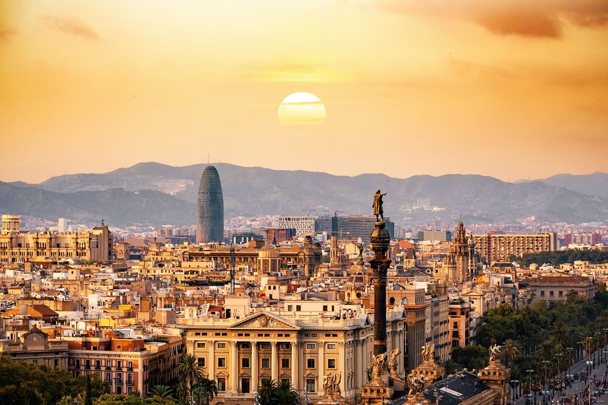Barcelona skyline at sunset with Sagrada Familia basilica and mountains in background under golden sky